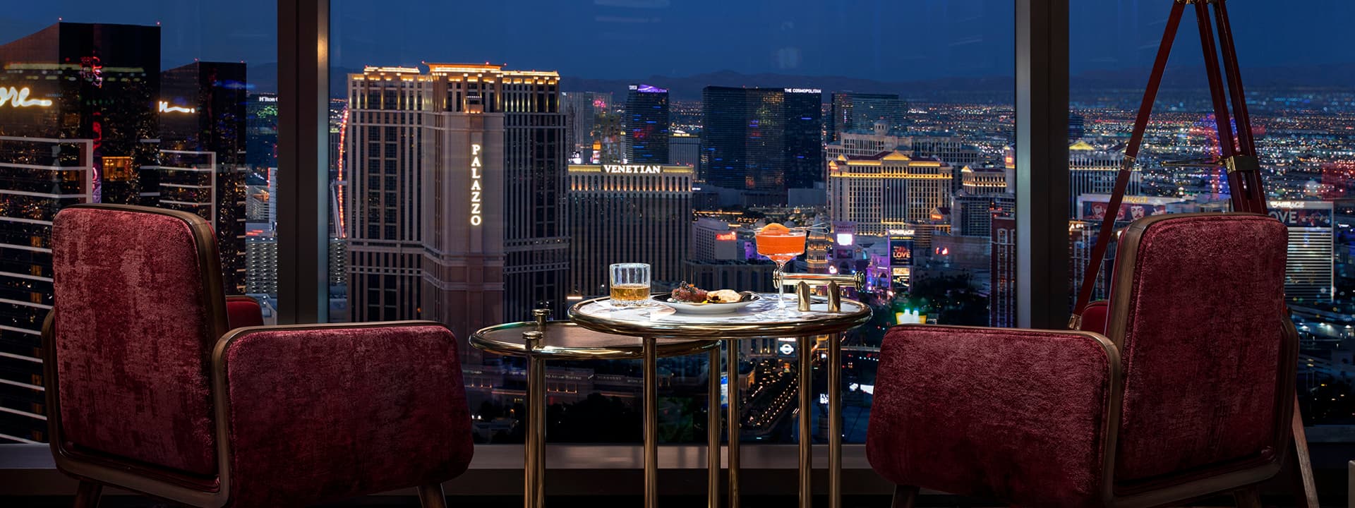 Cocktail table and lounge chairs overlooking the illuminated Las Vegas Strip at night from Allē Lounge on 66.