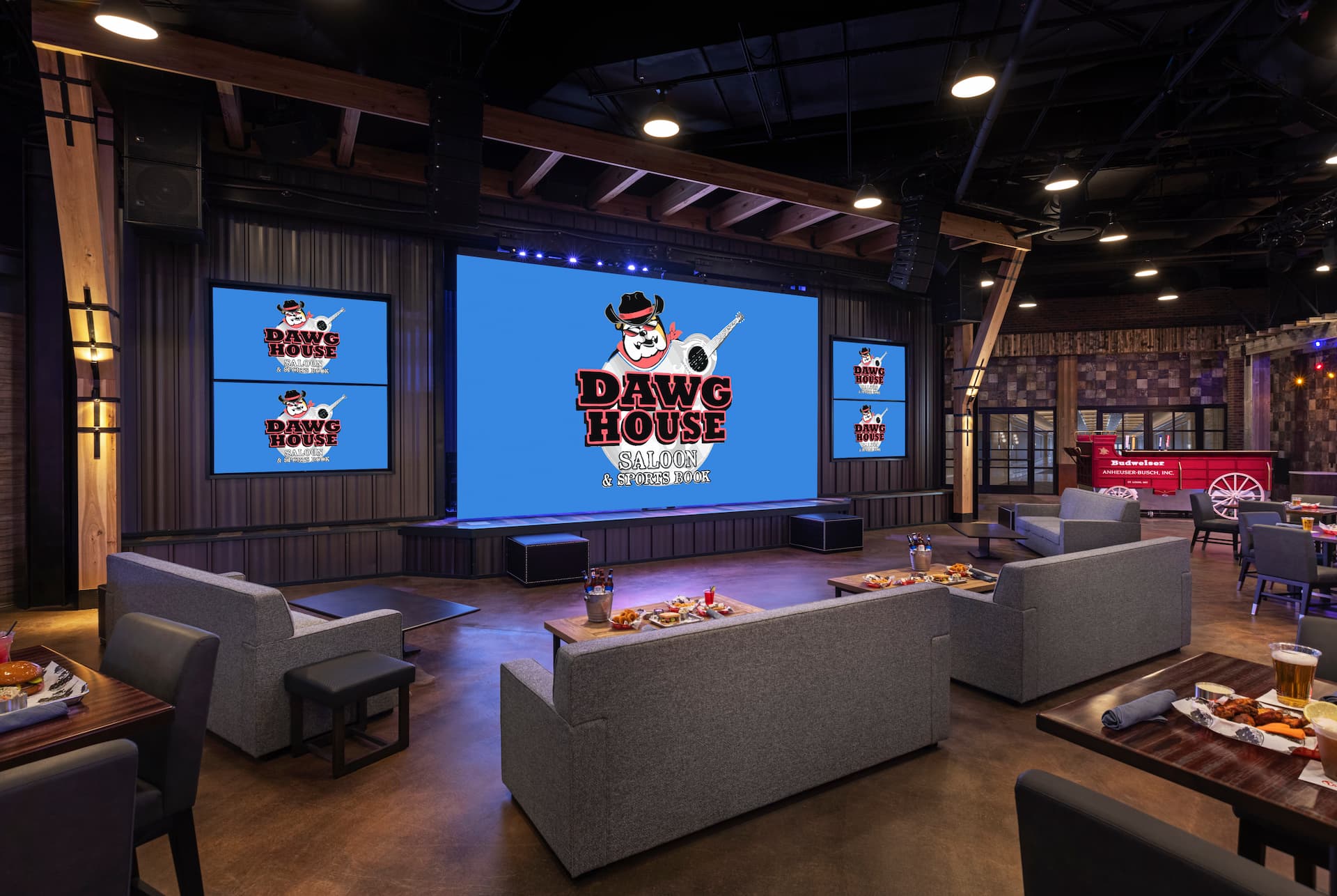 Dawg House Saloon & Sports Book interior with lounge seating, dining tables, a stage, and large digital screens.