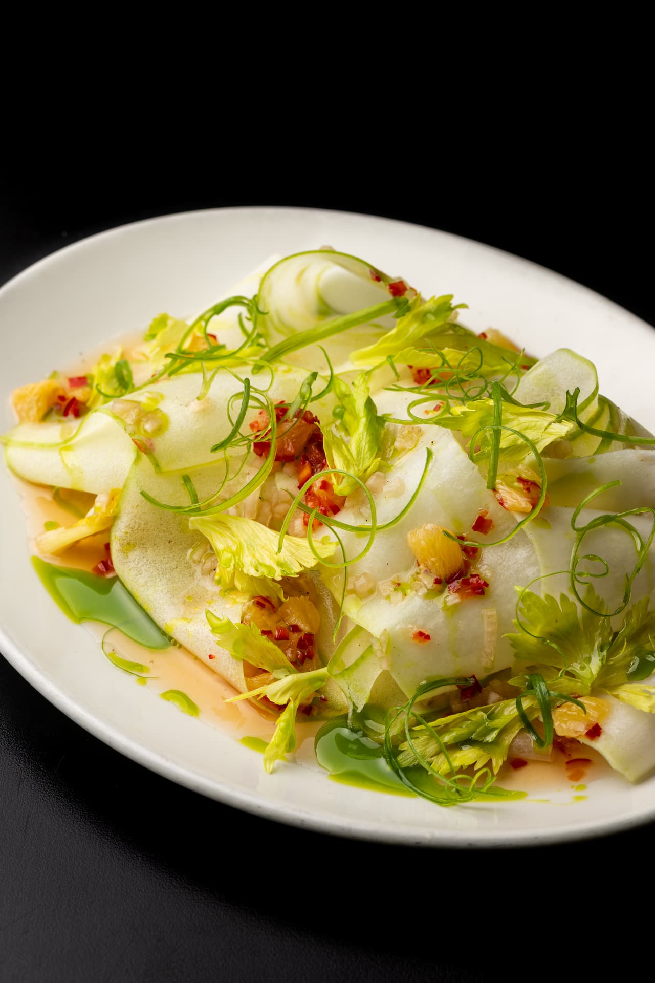 Thinly sliced green apples with celery leaves, fresh herbs, red pepper, and a light dressing served on a white plate.
