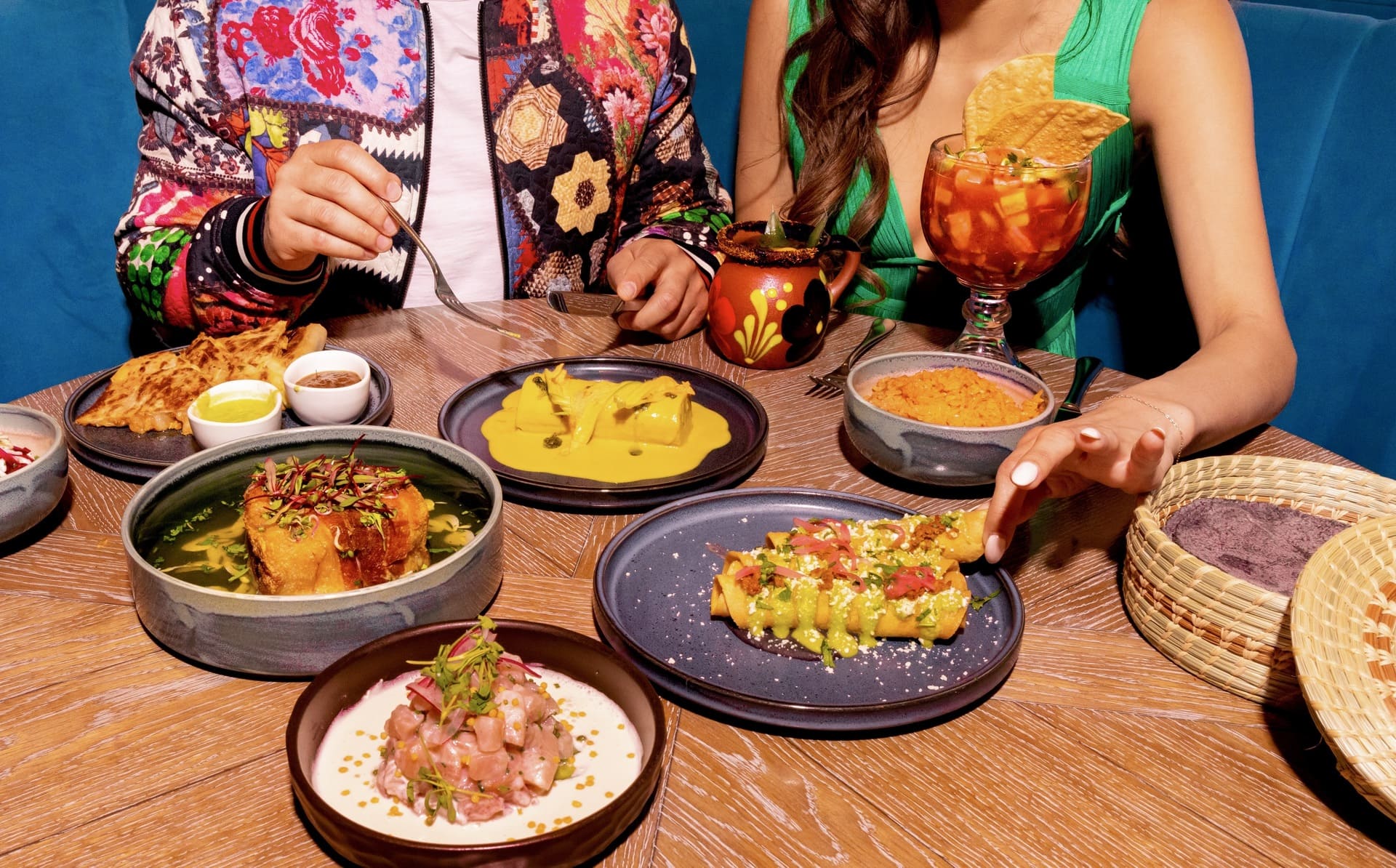 Couple enjoying a vibrant spread of upscale Latin cuisine, featuring colorful dishes, cocktails, and traditional tortillas.