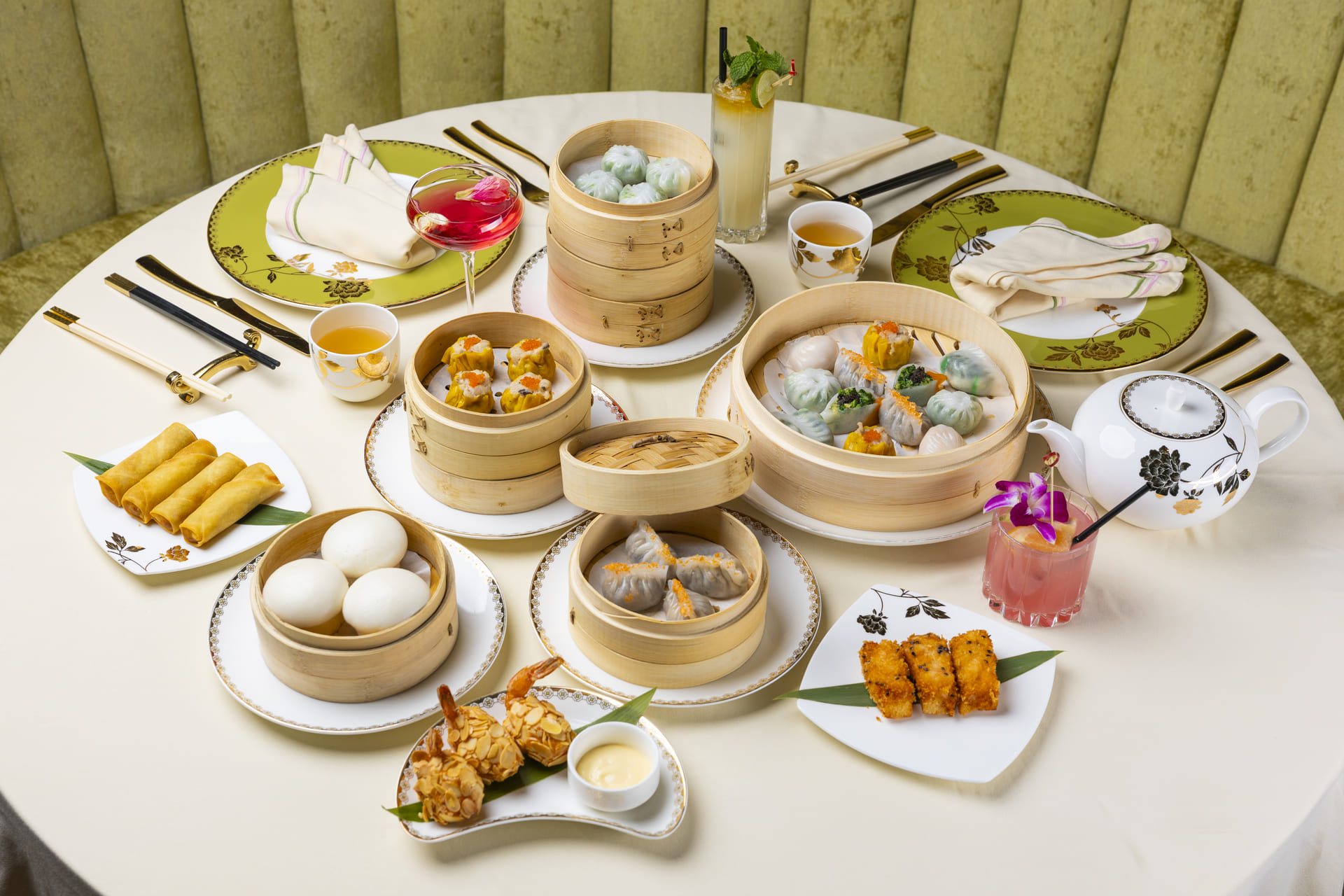 Dim sum lunch setting at Genting Palace with dumplings, spring rolls, cocktails, and tea on an elegant round table.