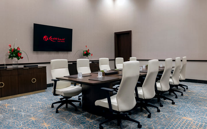 Modern boardroom with white chairs, dark table, and wall-mounted Resorts World Las Vegas screen.