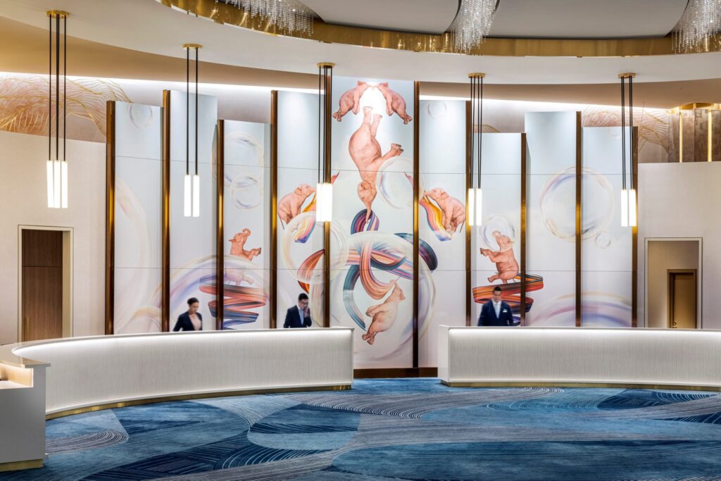 Modern hotel lobby with check-in desks and large colorful wall art behind staff