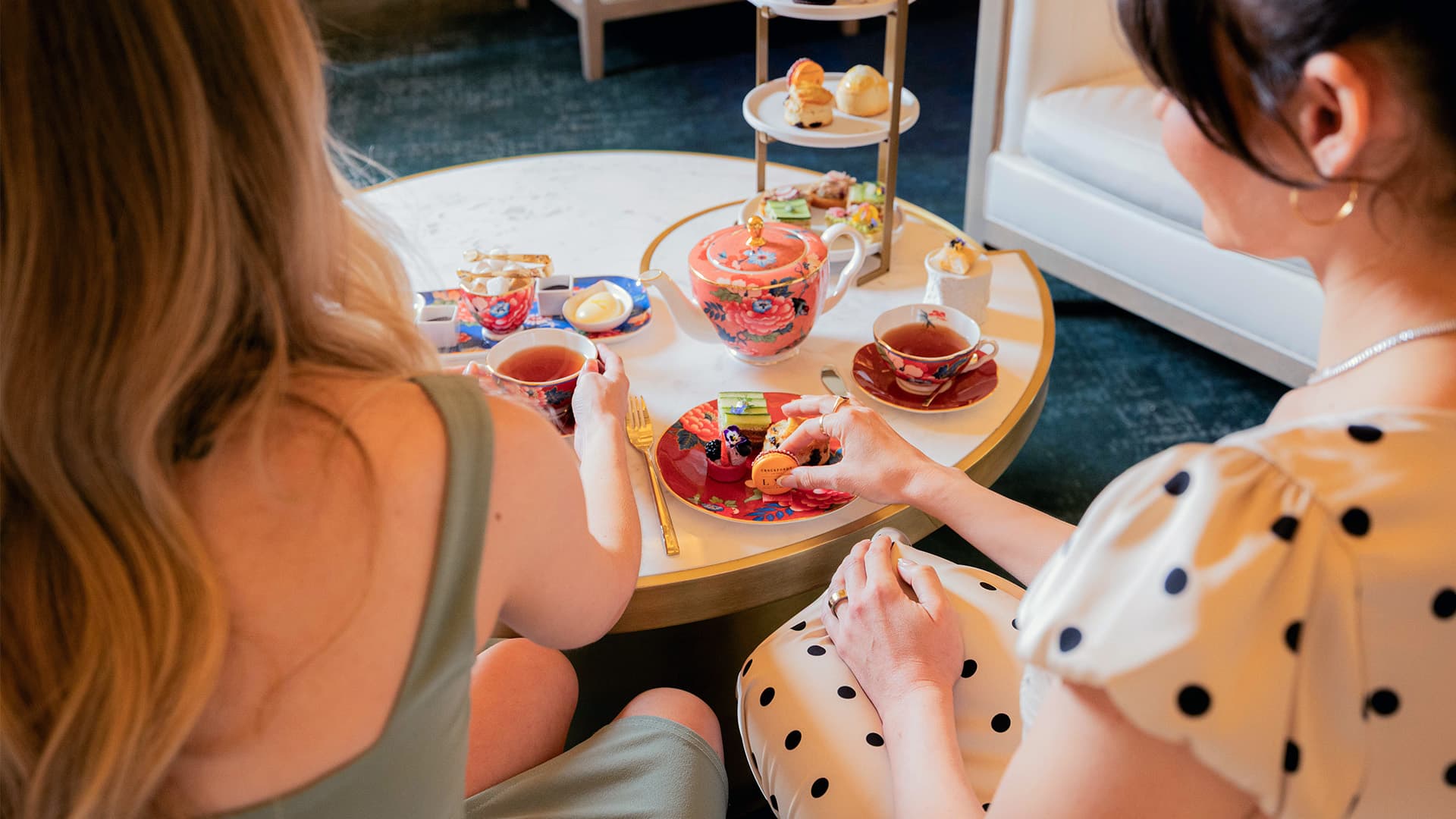 Two women enjoying tea and pastries at a table with teapot, cups, and dessert stand