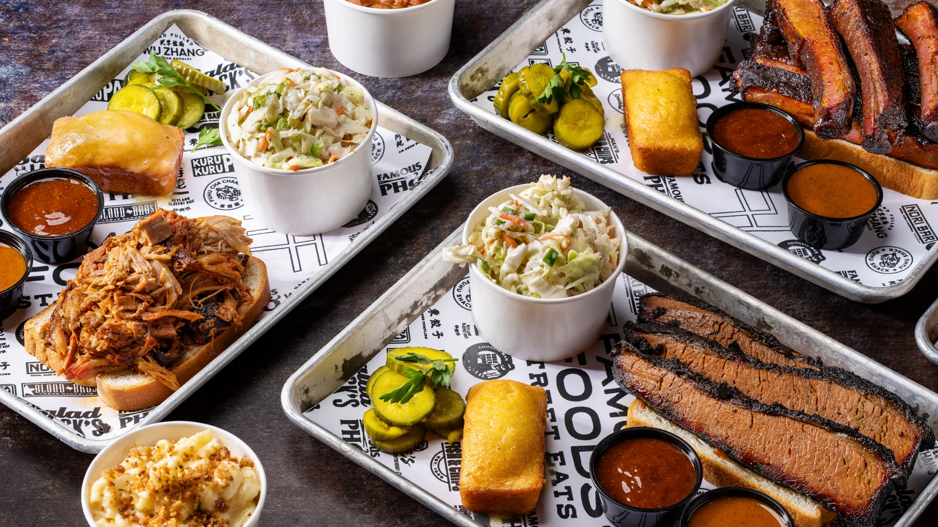 A selection of barbecue favorites including smoked brisket, pulled pork, pork ribs, coleslaw, cornbread, pickles, barbecue sauce, and macaroni and cheese displayed on Famous Foods serving trays.