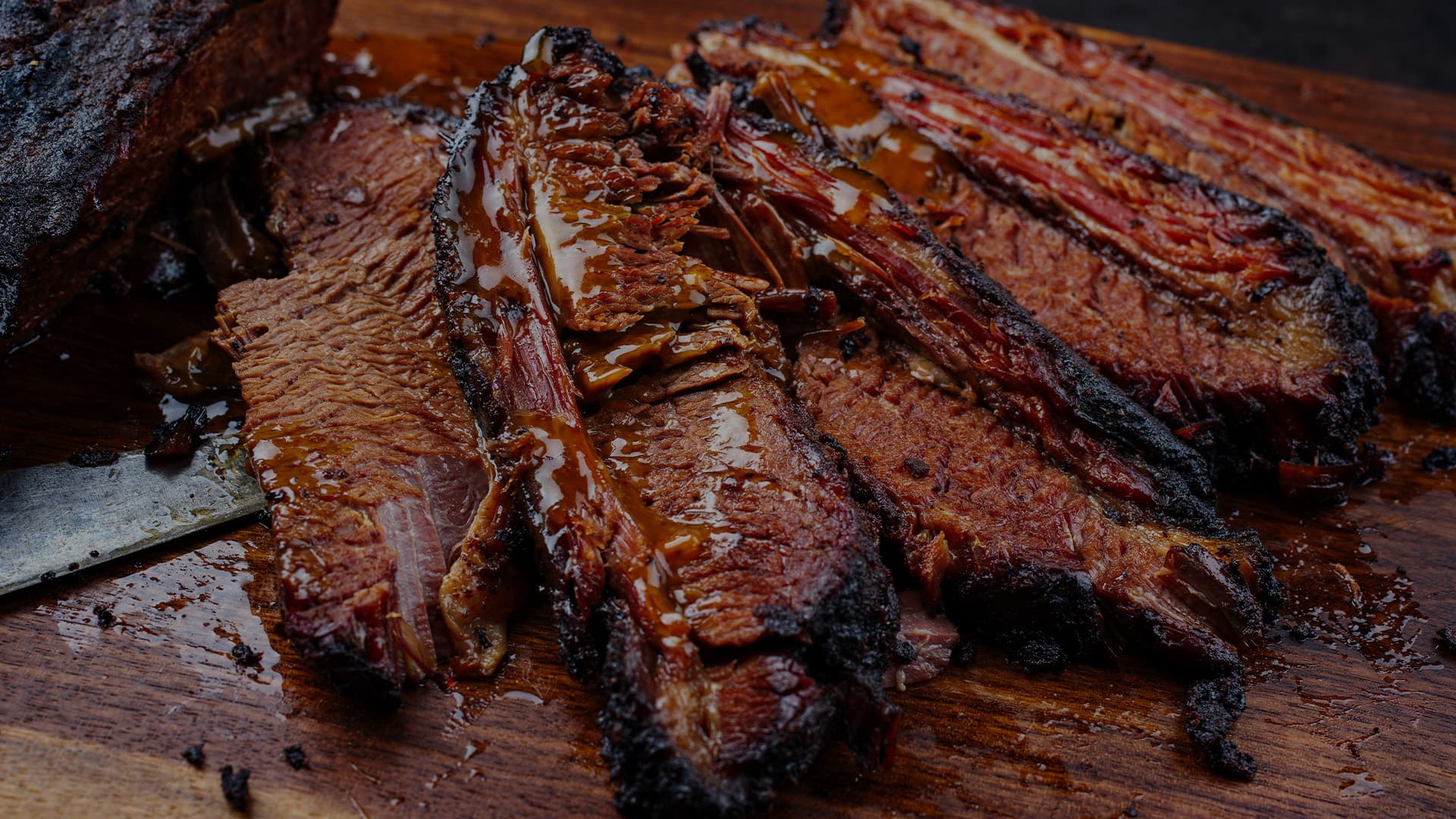 Close-up of smoked barbecue meats with sauce served on a wooden cutting board.