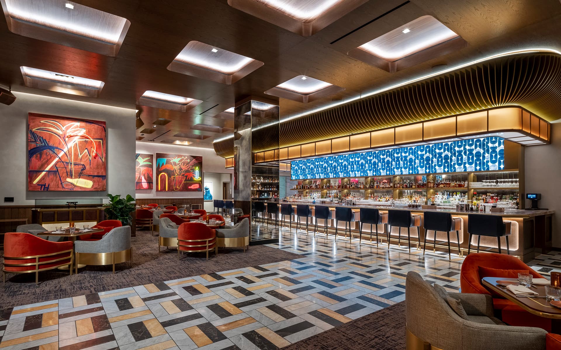 Upscale restaurant lounge with a long illuminated bar, modern seating, contemporary artwork, and warm ambient lighting.