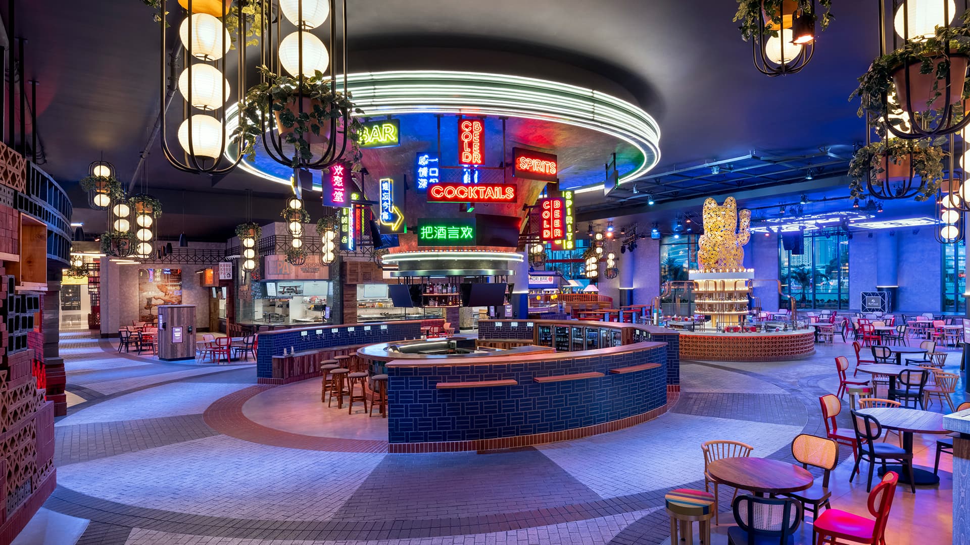 Wide view of Famous Foods Street Eats featuring a circular central bar, colorful neon signage, food vendor counters, hanging lantern-style lighting, and open dining seating.