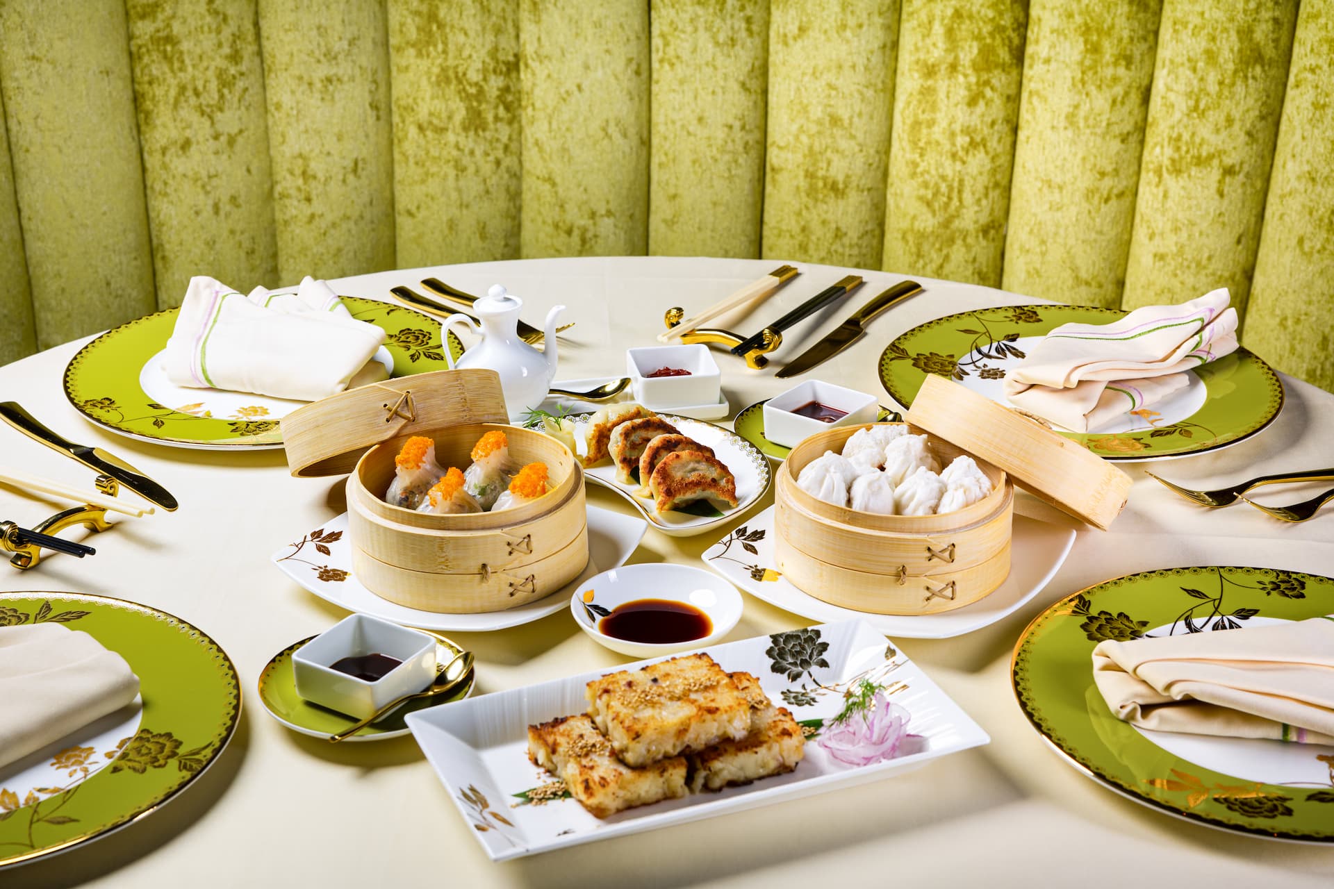 Elegant dining table at Genting Palace featuring dim sum baskets, dumplings, pan-fried appetizers, dipping sauces, fine table settings, and decorative green-and-gold dinnerware.