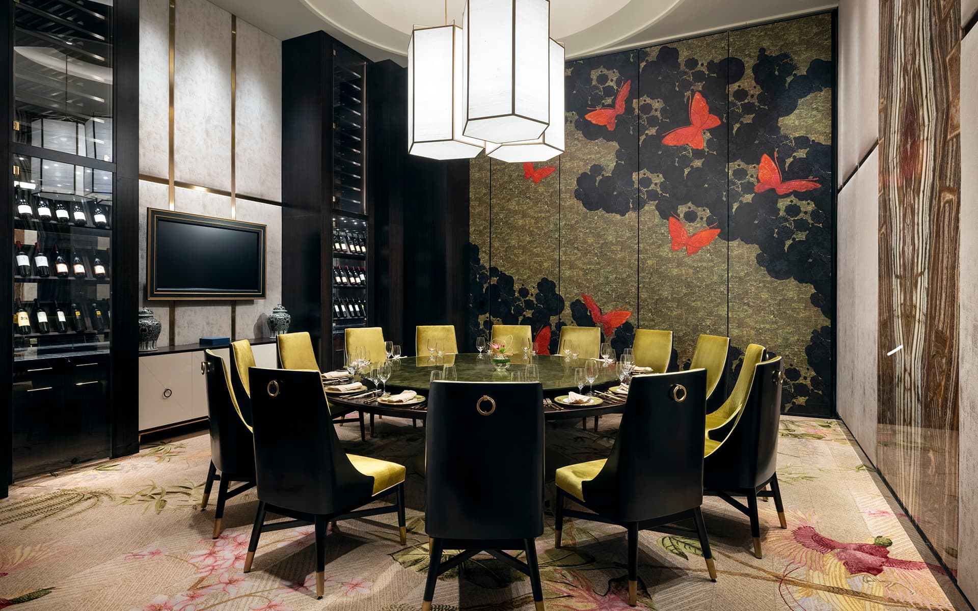Elegant private dining room with a round table, upholstered chairs, floral-patterned carpet, and decorative butterfly wall mural.