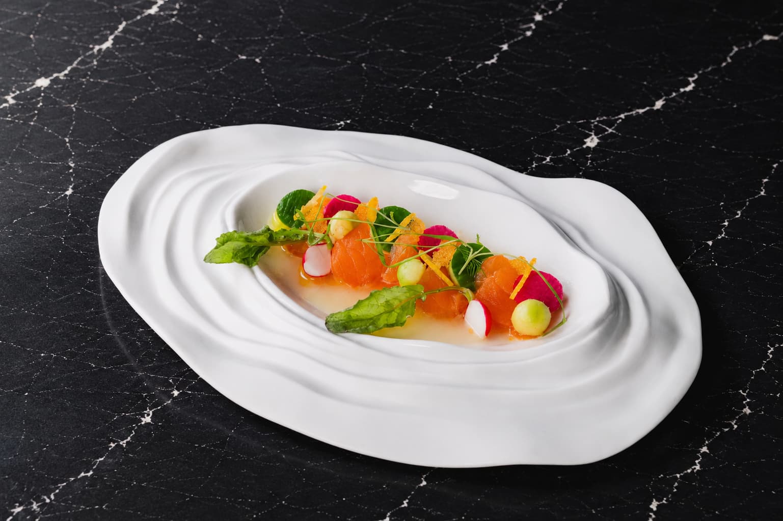 Elegant salmon sashimi presentation with Scottish salmon, yuzu accents, radish slices, melon pearls, microgreens, and citrus dressing served on a sculpted white plate.