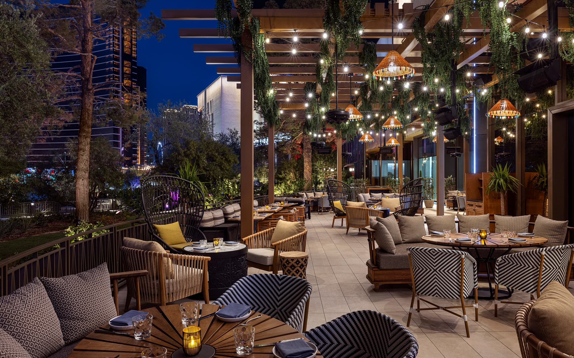 Outdoor patio dining area at Viva! featuring lounge seating, hanging greenery, string lights, and illuminated décor in an evening garden setting.