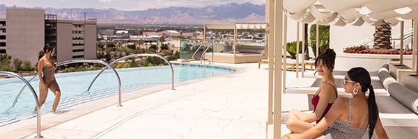 Guests relax beside an infinity pool overlooking the Las Vegas skyline and surrounding mountains from a rooftop terrace.