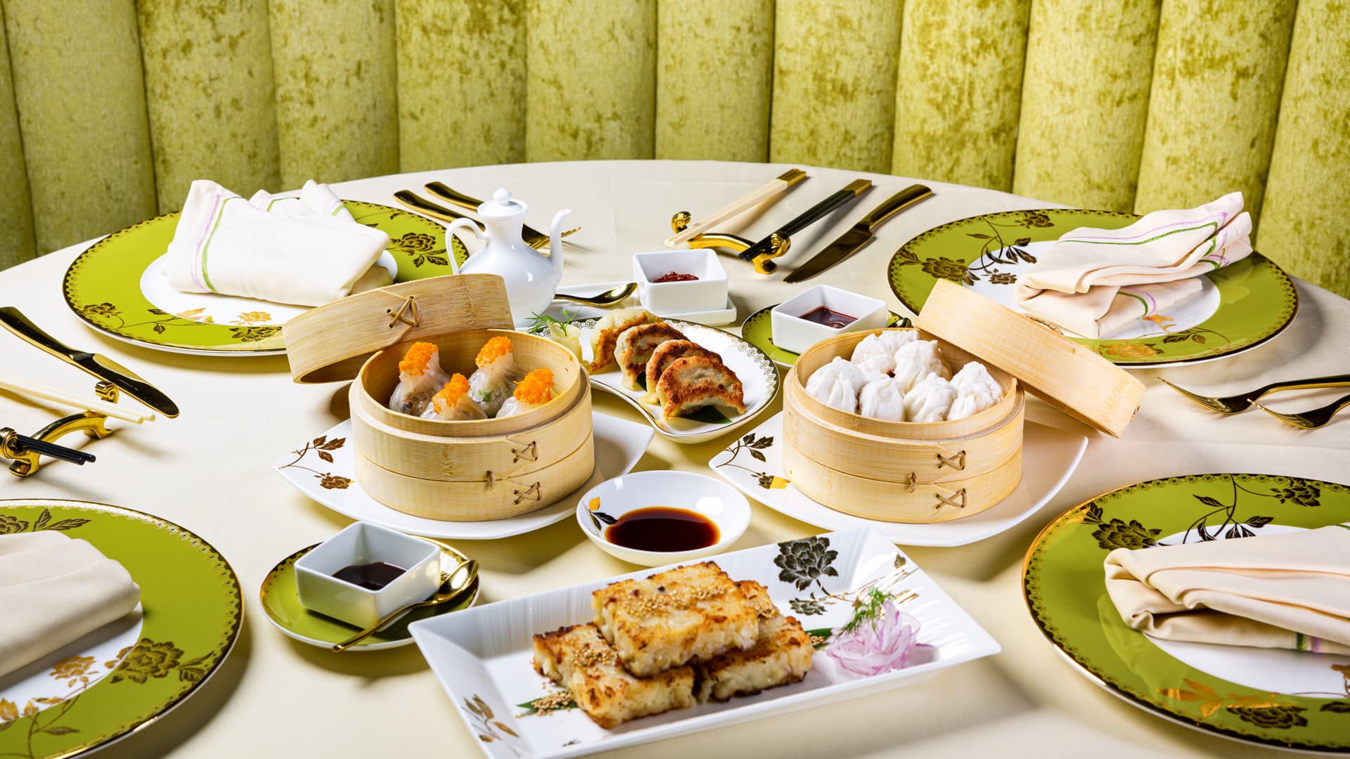 A table at Genting Palace featuring dim sum baskets, pan-fried dumplings, crispy seafood cakes, dipping sauces, and traditional Chinese table settings prepared for a shared dining experience.