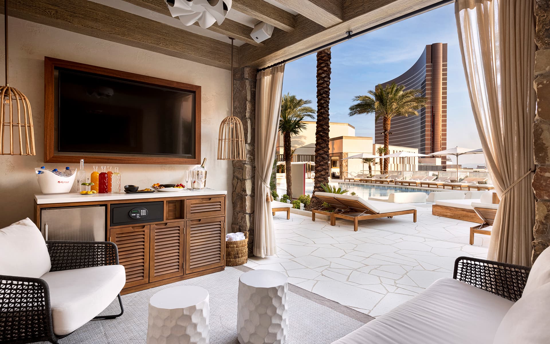 Interior of a private VIP pool cabana at Resorts World Las Vegas featuring lounge seating, a television, refreshments, and an open-air view of the pool deck and hotel tower.