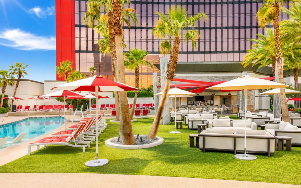 Bimini Pool at Resorts World Las Vegas with red lounge chairs, shaded seating, palm trees, and poolside cabanas.