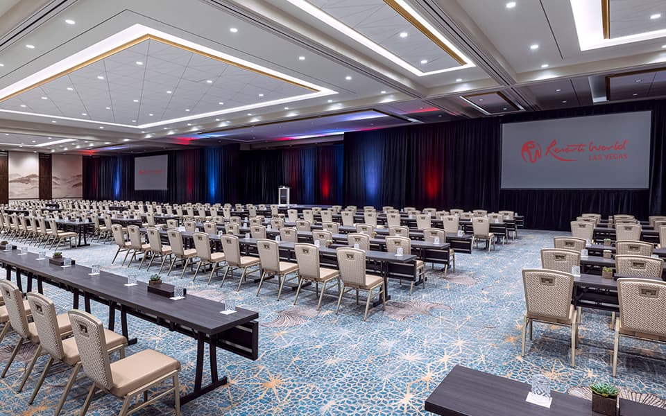 Blossom Ballroom at Resorts World Las Vegas arranged in a classroom-style setup with rows of tables and chairs facing presentation screens.