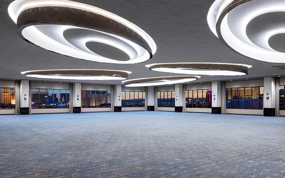 Spacious conference room with modern circular ceiling lights, floor-to-ceiling windows, and views of the Las Vegas skyline.