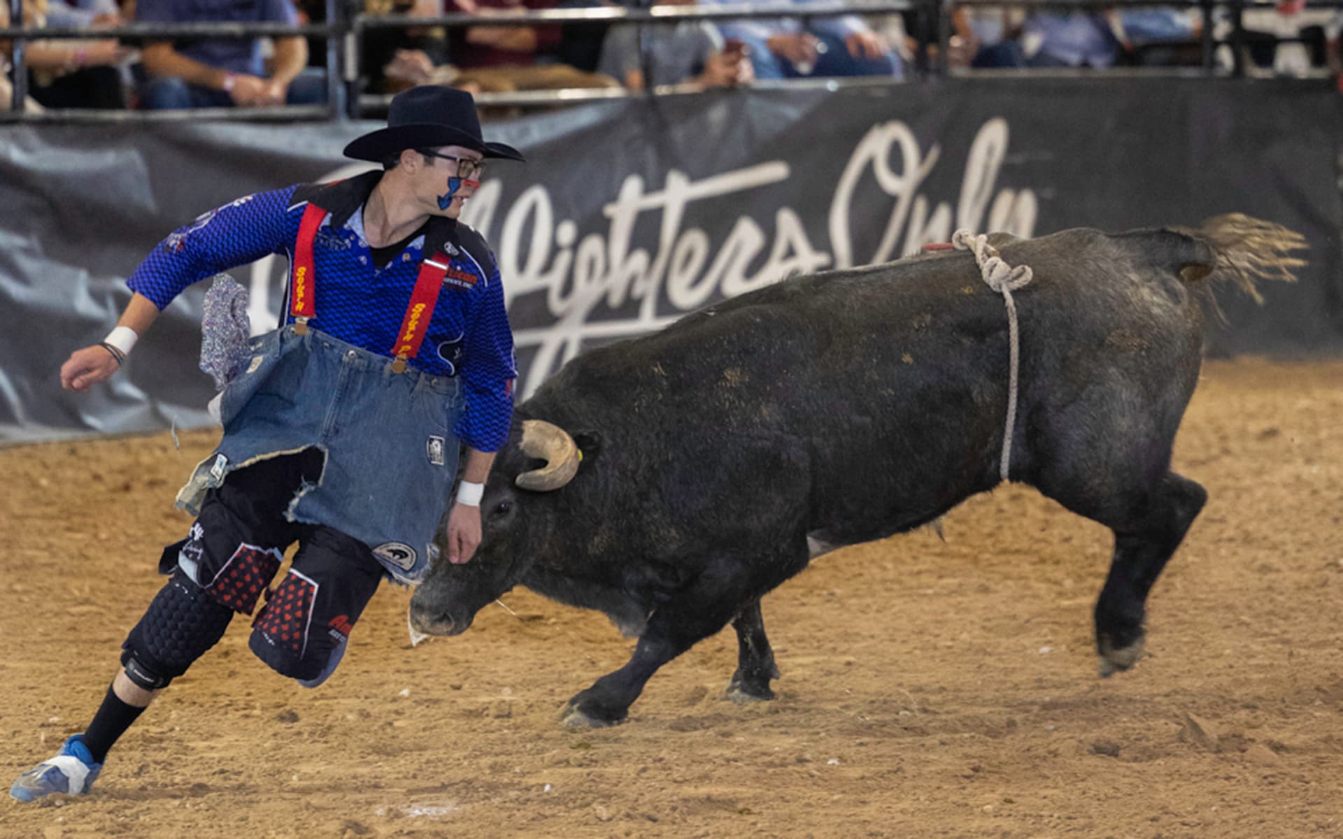 Rodeo bullfighter moves alongside a charging bull during an action-filled event in the arena.