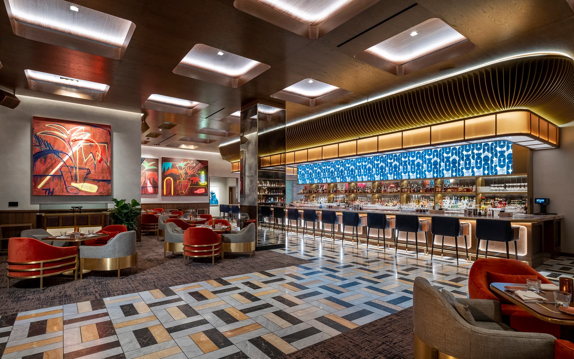 Interior of Carversteak featuring a modern bar, lounge seating, colorful artwork, and geometric flooring.