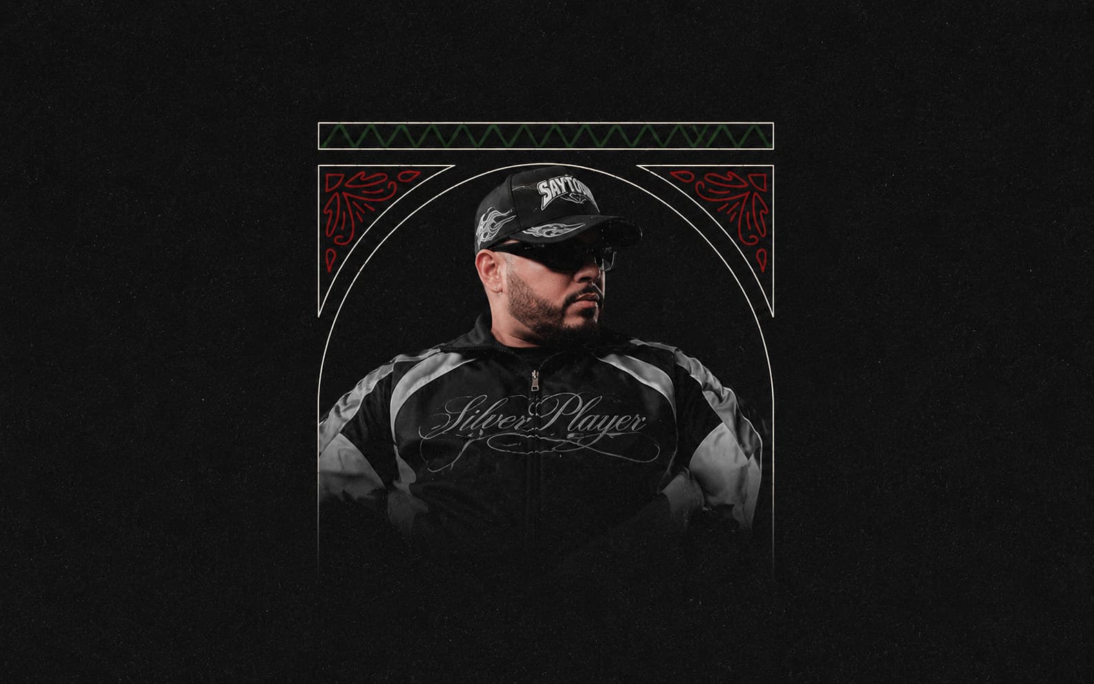 Portrait of Dynamiq wearing sunglasses, a black cap, and a black jacket against a dark decorative background.
