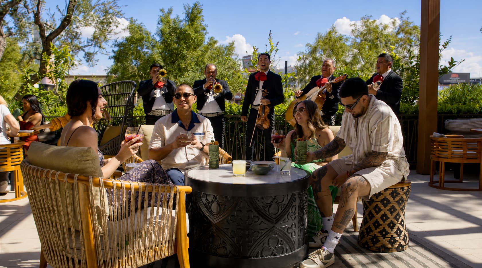 Guests enjoy drinks at an outdoor dining patio while a mariachi band performs nearby.