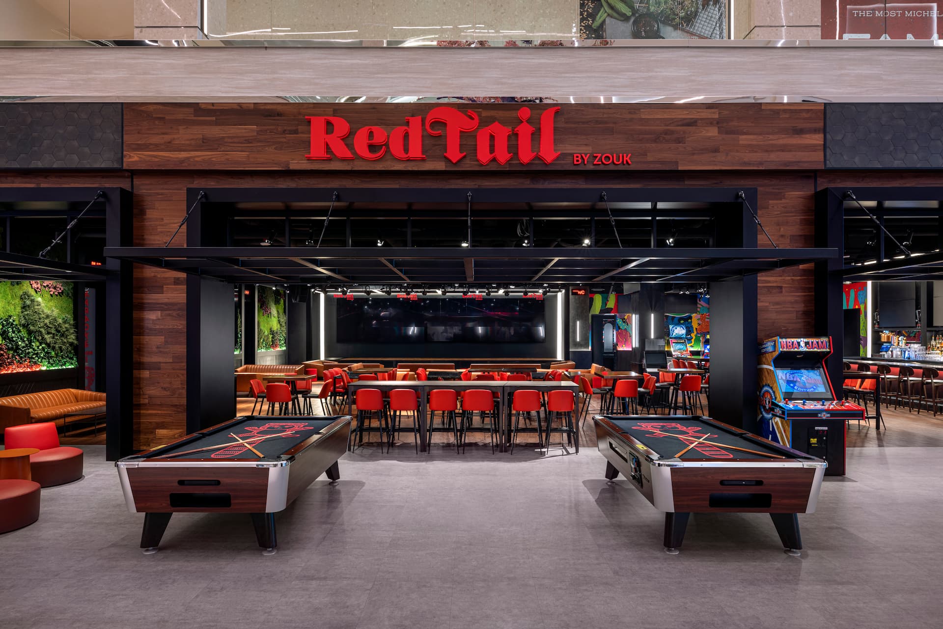 Interior of RedTail by Zouk featuring game tables, arcade machines, red seating, and a spacious sports bar area.