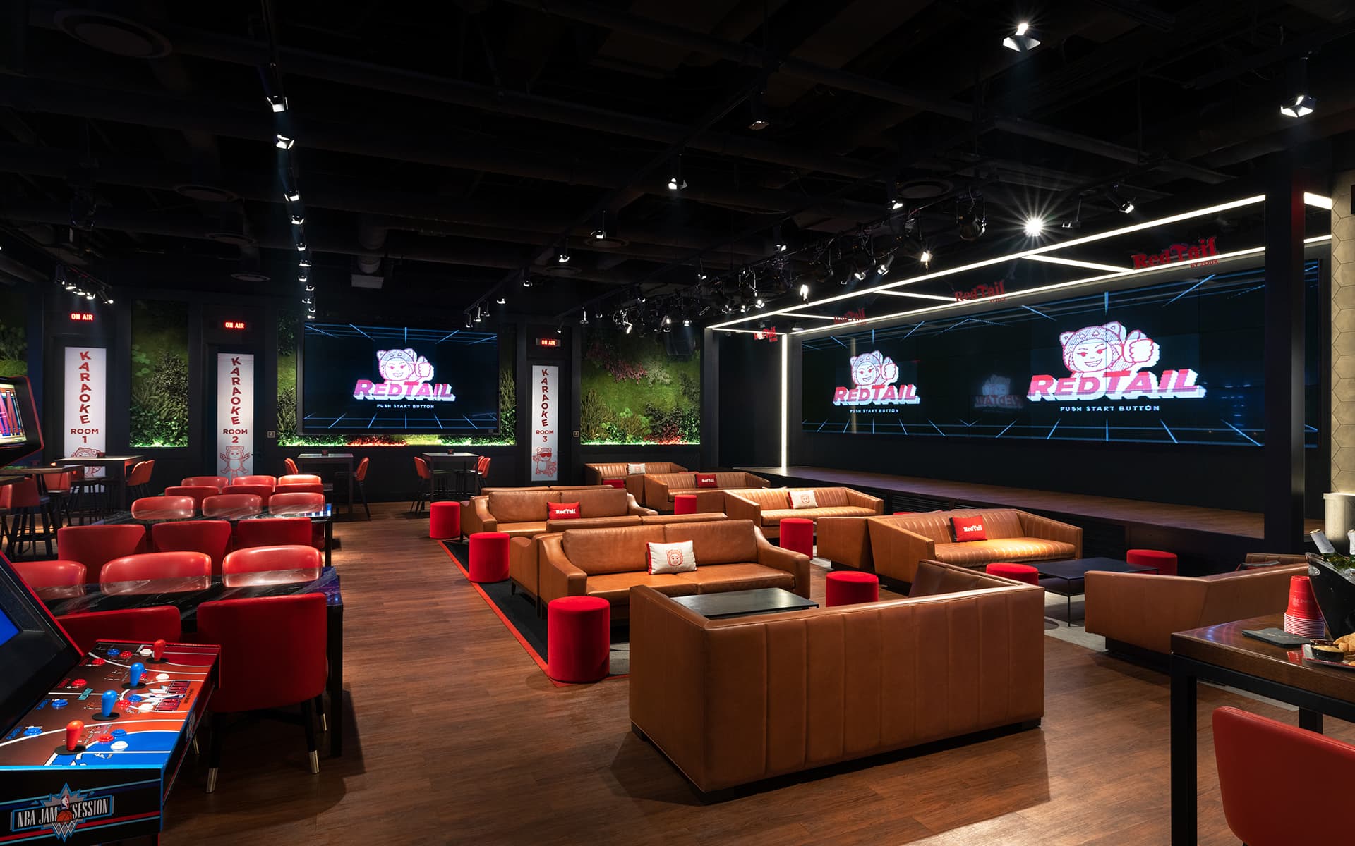 Interior of RedTail featuring lounge seating, large video screens, karaoke rooms, and arcade games.