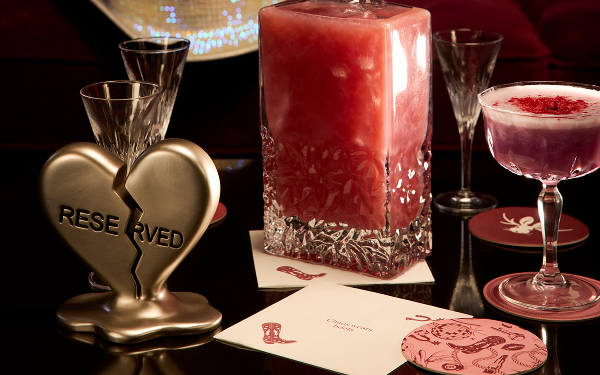 Pink cocktails displayed on a lounge table beside a gold broken-heart Reserved sign and decorative coasters.