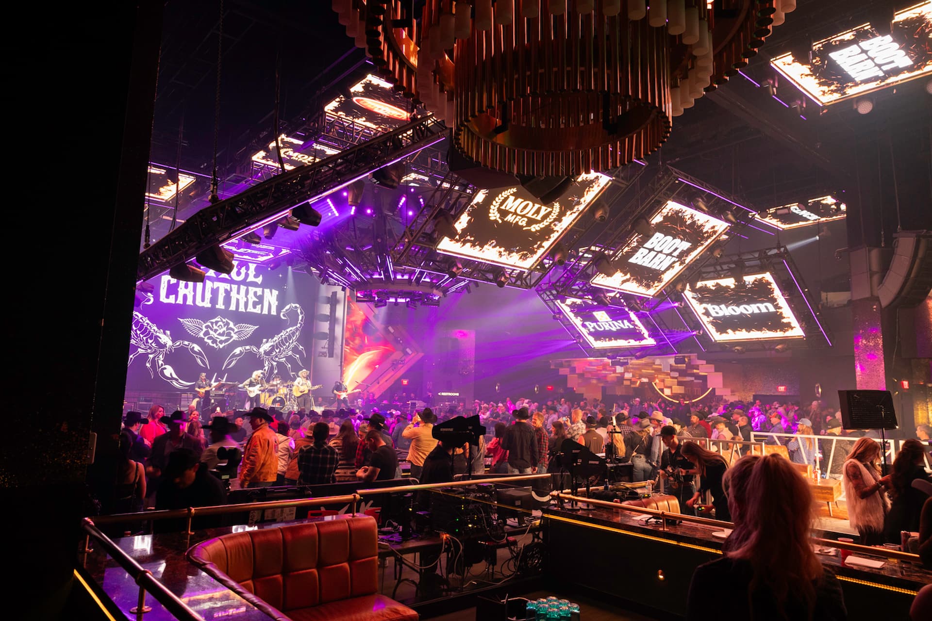 Live band performing for a large crowd under purple stage lighting and suspended digital screens at Resorts World.