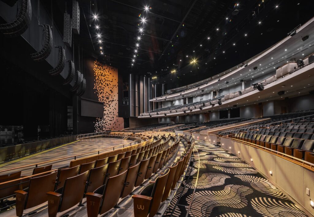 Interior of Resorts World Theatre in Las Vegas featuring tiered seating, balconies, stage, and overhead lighting.